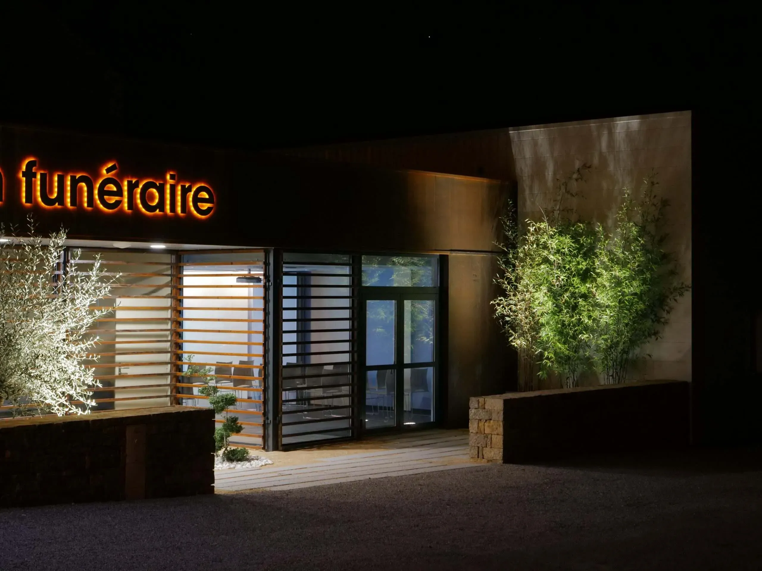 Entrée de nuit de la maison funéraire avec enseigne lumineuse orange et bambous.