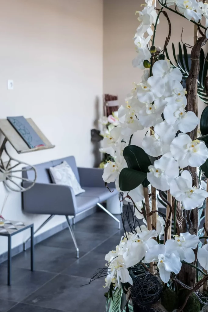 Salon d'accueil funéraire avec canapé gris et grand bouquet d'orchidées blanches.