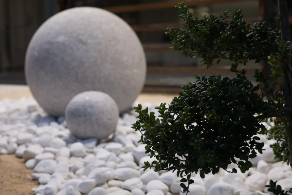 Jardin zen funéraire avec sphères en pierre, gravier blanc et arbuste taillé.