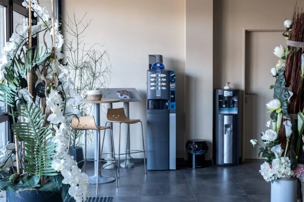 Espace détente avec distributeur de café, fontaine à eau et coin table haute.